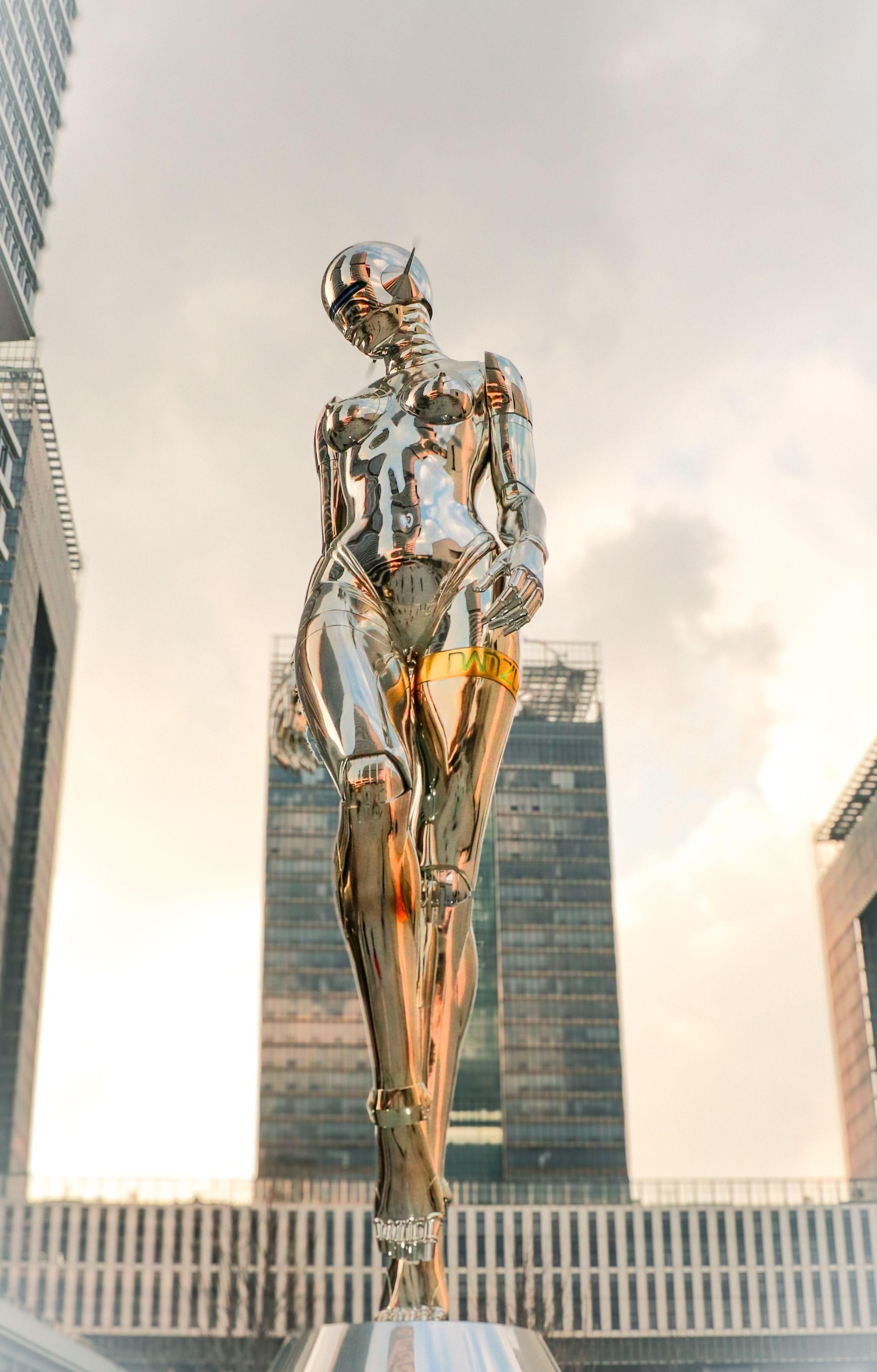 A chrome-finished humanoid robot standing in an urban plaza